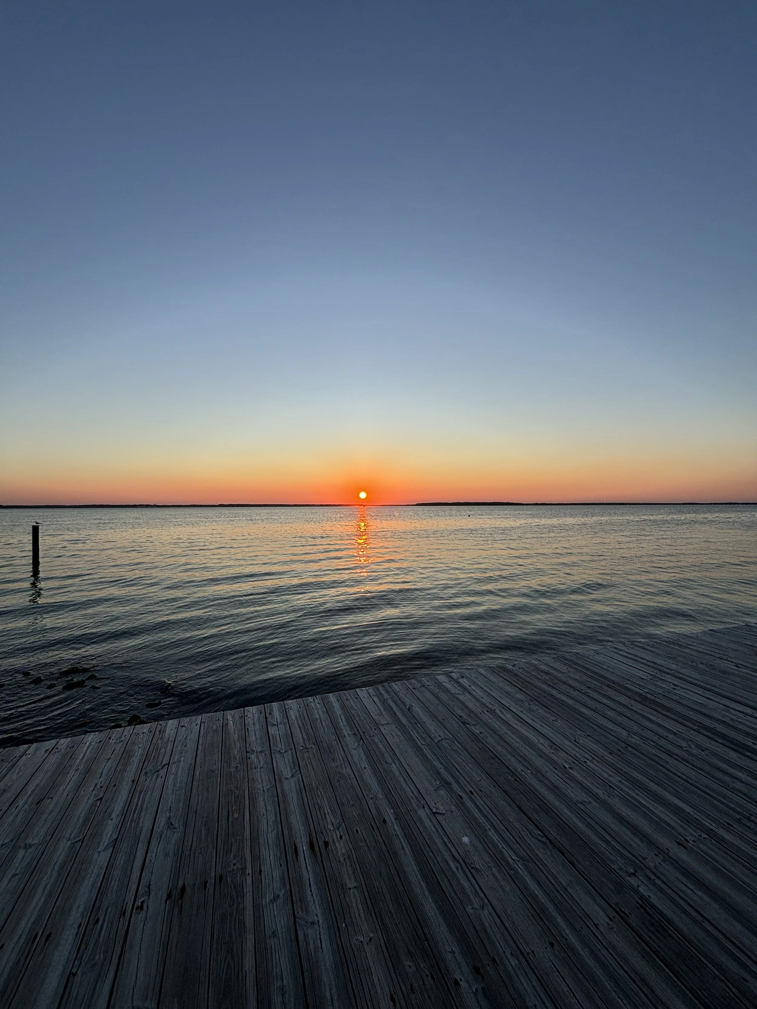 Sunset over a calm body of water viewed from a wooden dock.