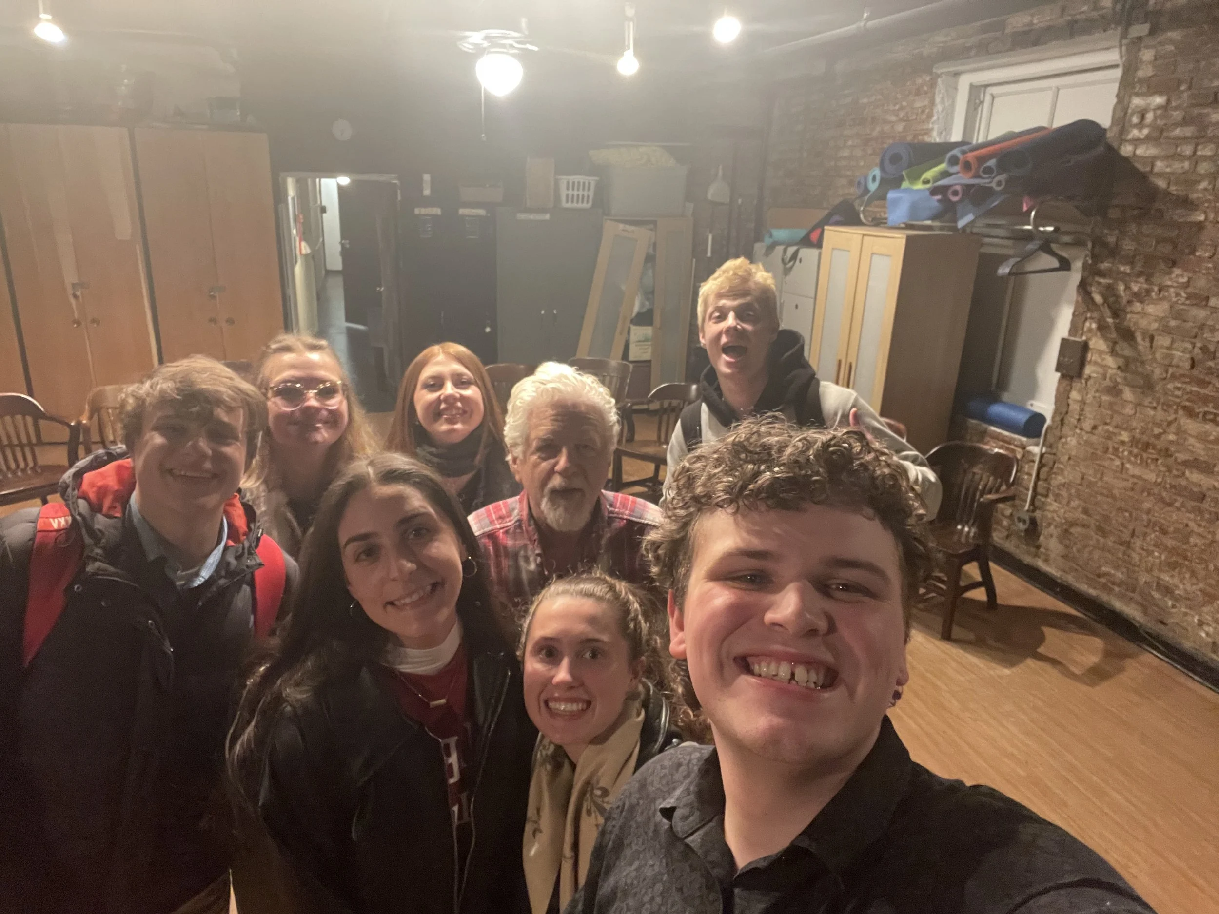 A group of nine people smiling and posing for a photo indoors with brick walls and wooden furniture.