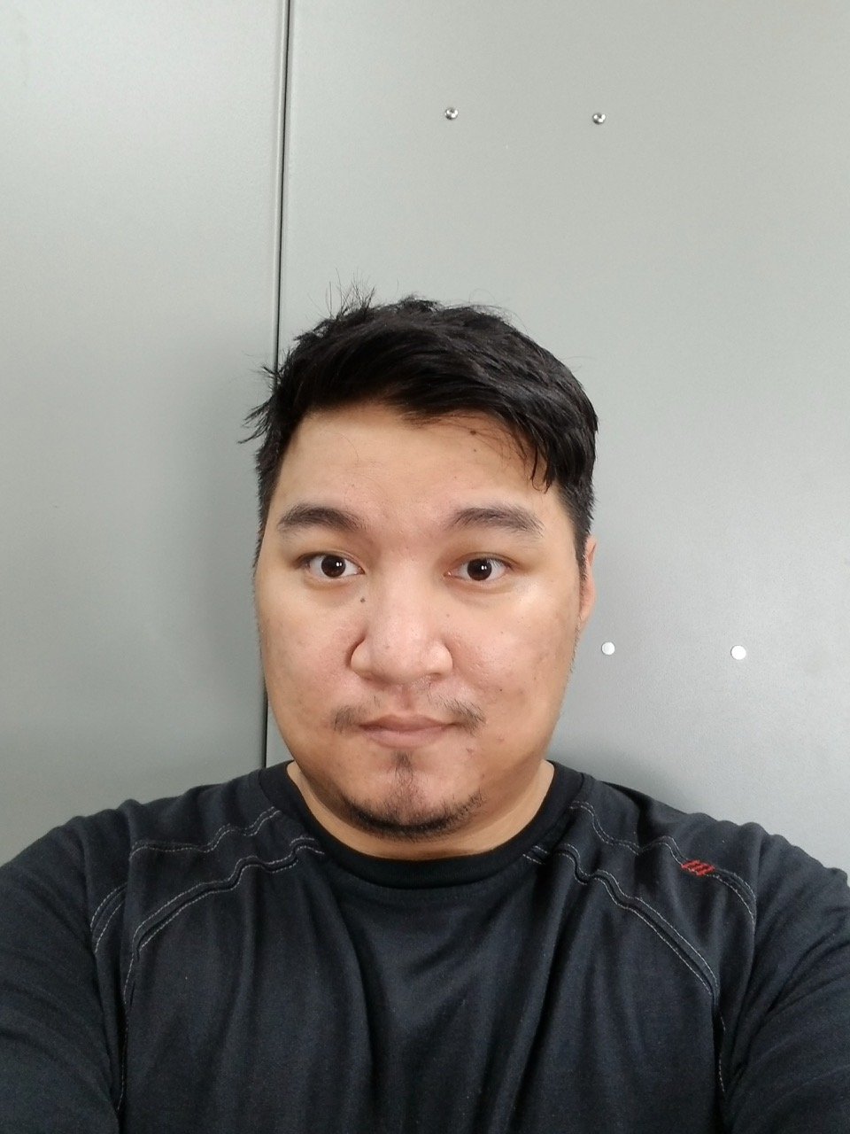 A man taking a selfie in front of a plain gray wall.