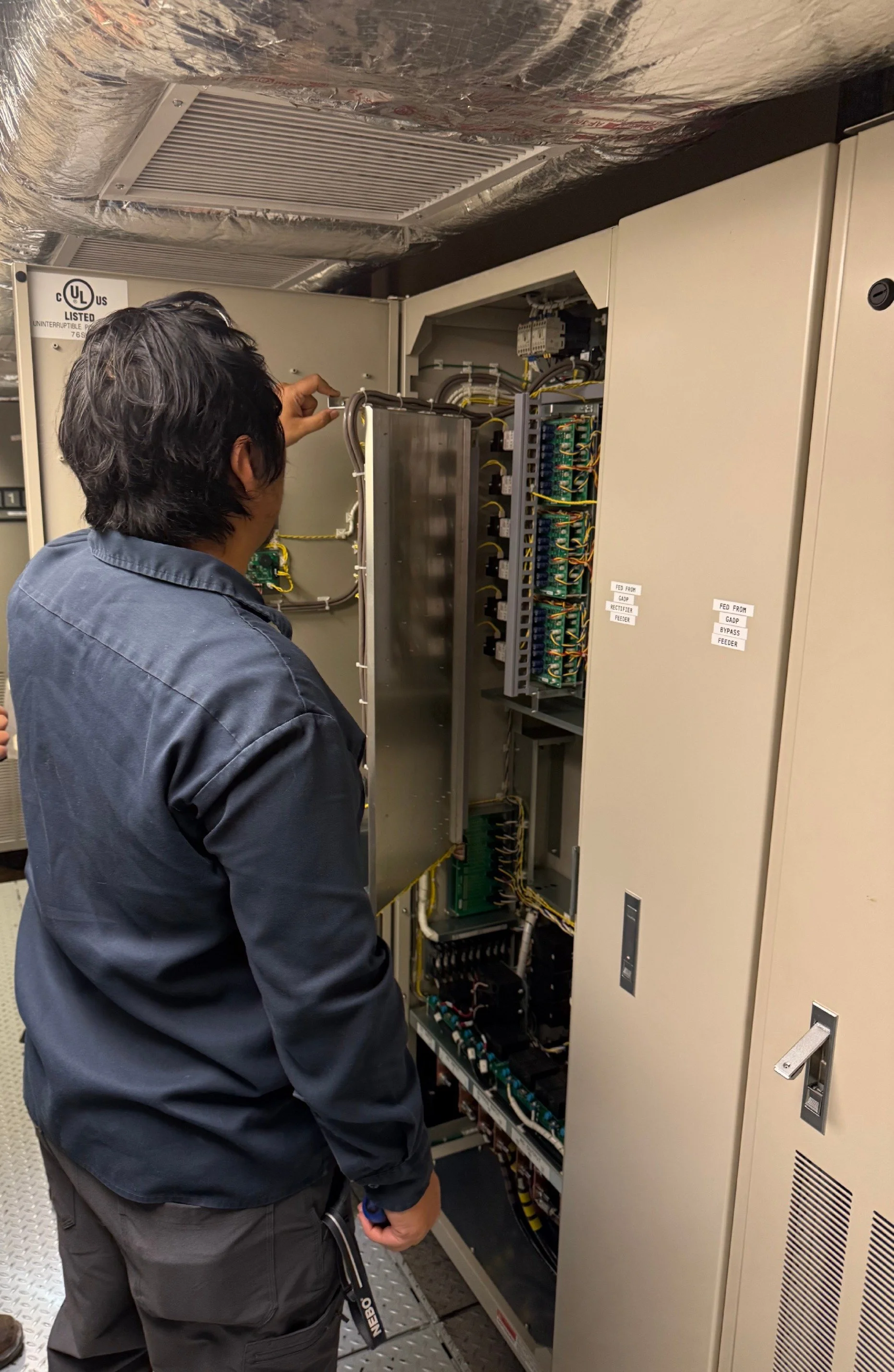 A technician working on an electrical control panel inside an industrial or commercial building.