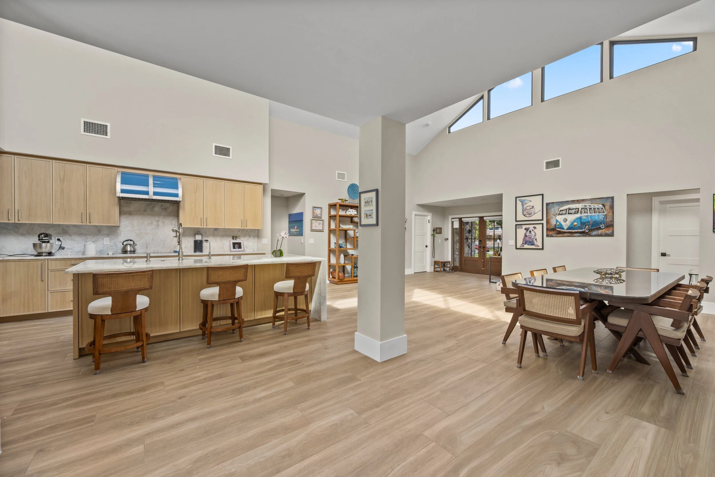 Open concept living room and kitchen with high vaulted ceiling, wooden flooring, wall art, and a dining table.