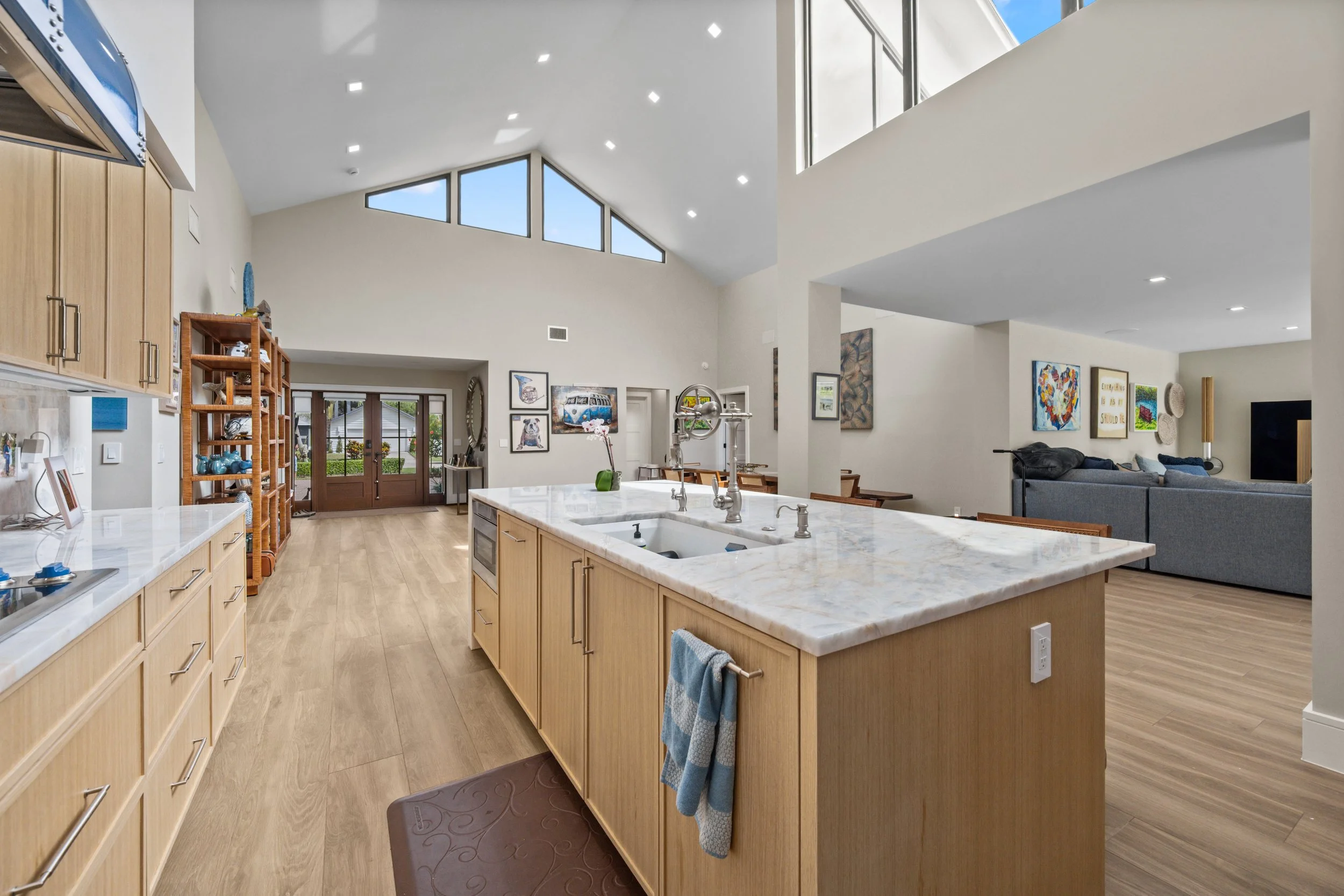 Open-concept kitchen and living room with high vaulted ceiling, large windows, and artwork on the walls.