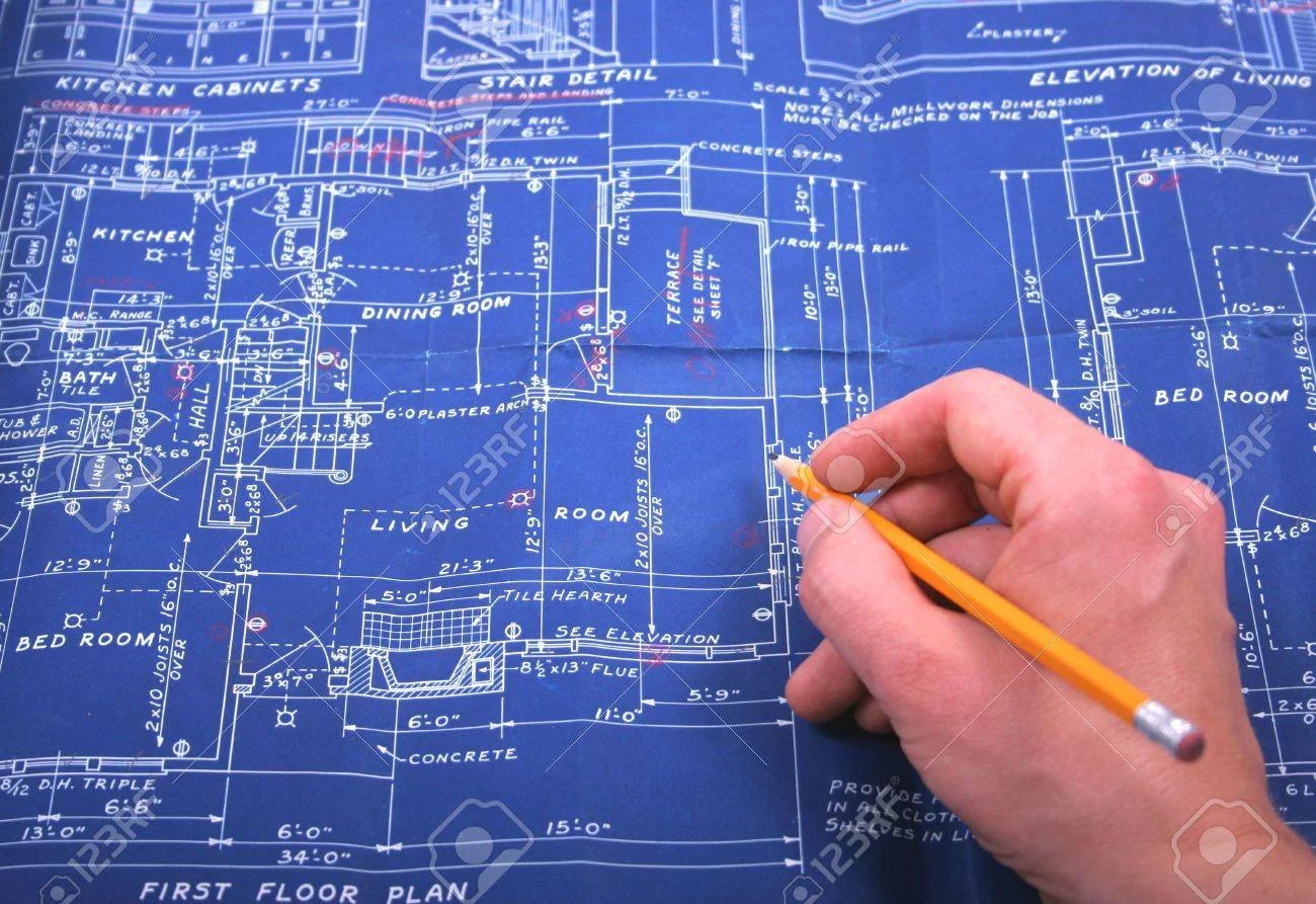 Blueprints of a house with a person holding a pencil drawing on the floor plan.
