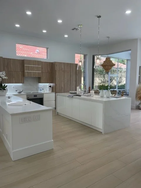 Modern kitchen with white island, wooden cabinets, and large windows with views of trees.