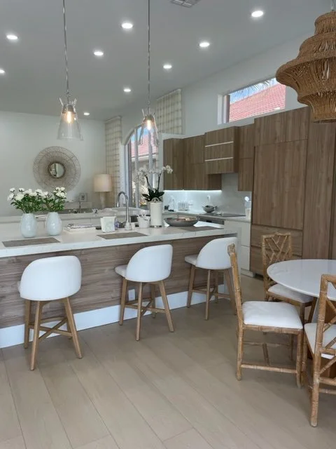 Modern kitchen and dining area with white and wood decor, three white bar stools at the kitchen island, and a round dining table with wooden chairs.