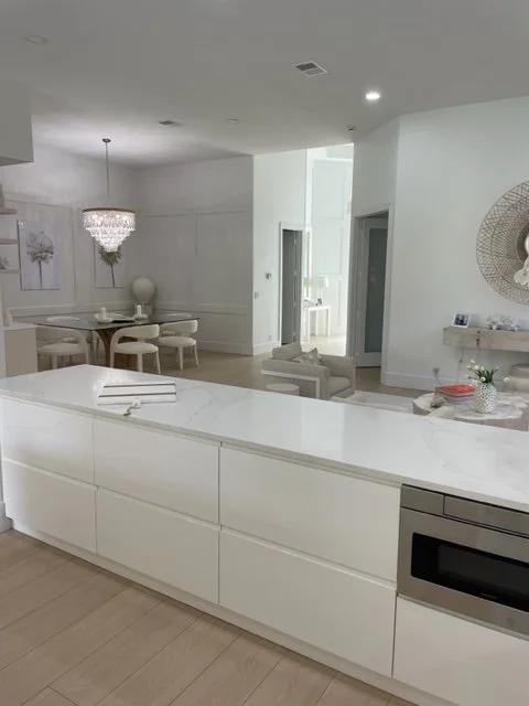 Modern kitchen and dining area with white cabinetry, a microwave, dining table, chandelier, and decorative wall art.