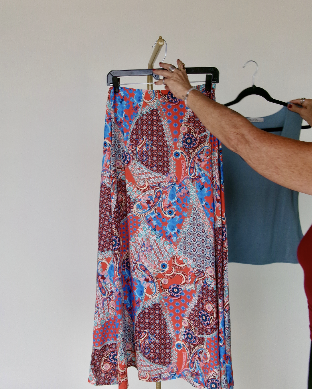 A person hanging a colorful, patterned skirt on a clothing rack.