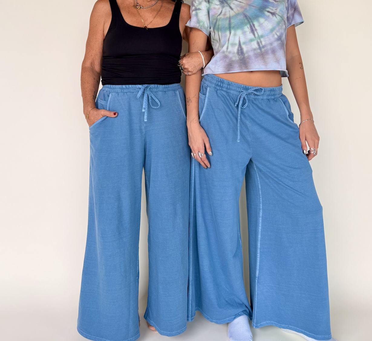 Two women standing side by side wearing loose-fitting, wide-leg blue jeans and casual tops, against a plain white background.