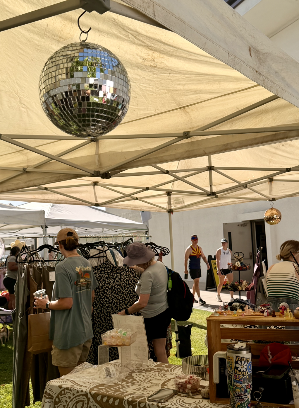A disco ball hanging from a canopy at an outdoor market with people shopping and browsing stalls.