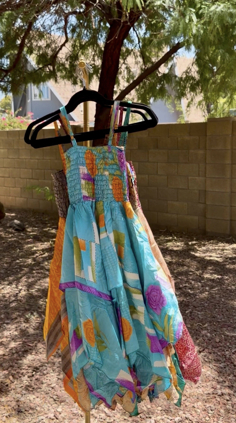Colorful dress hanging on a black hanger, outdoors with a brick wall and tree in the background.