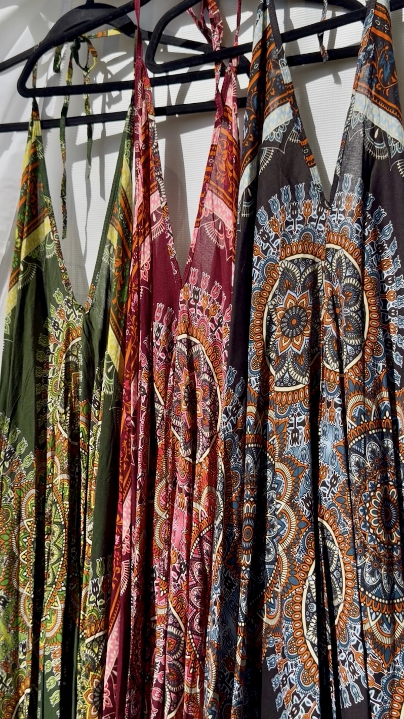 Colorful patterned dresses hanging on black hangers on a rack.