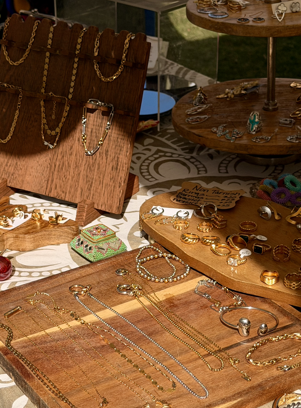 Display of gold and silver jewelry on wooden stands and trays, including necklaces, rings, bracelets, and earrings.
