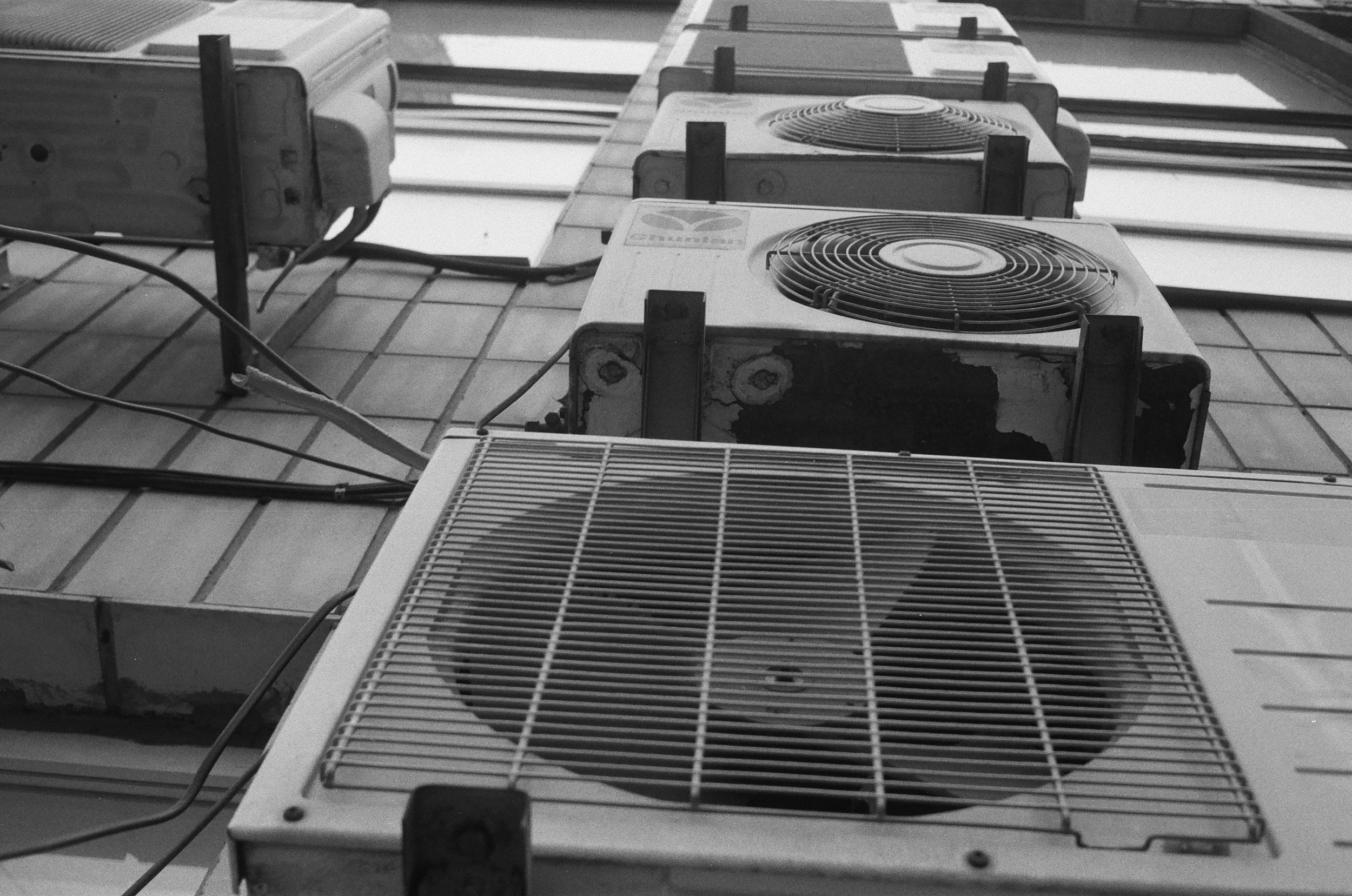 Black and white photo of several outdoor air conditioning units mounted on a tiled wall.