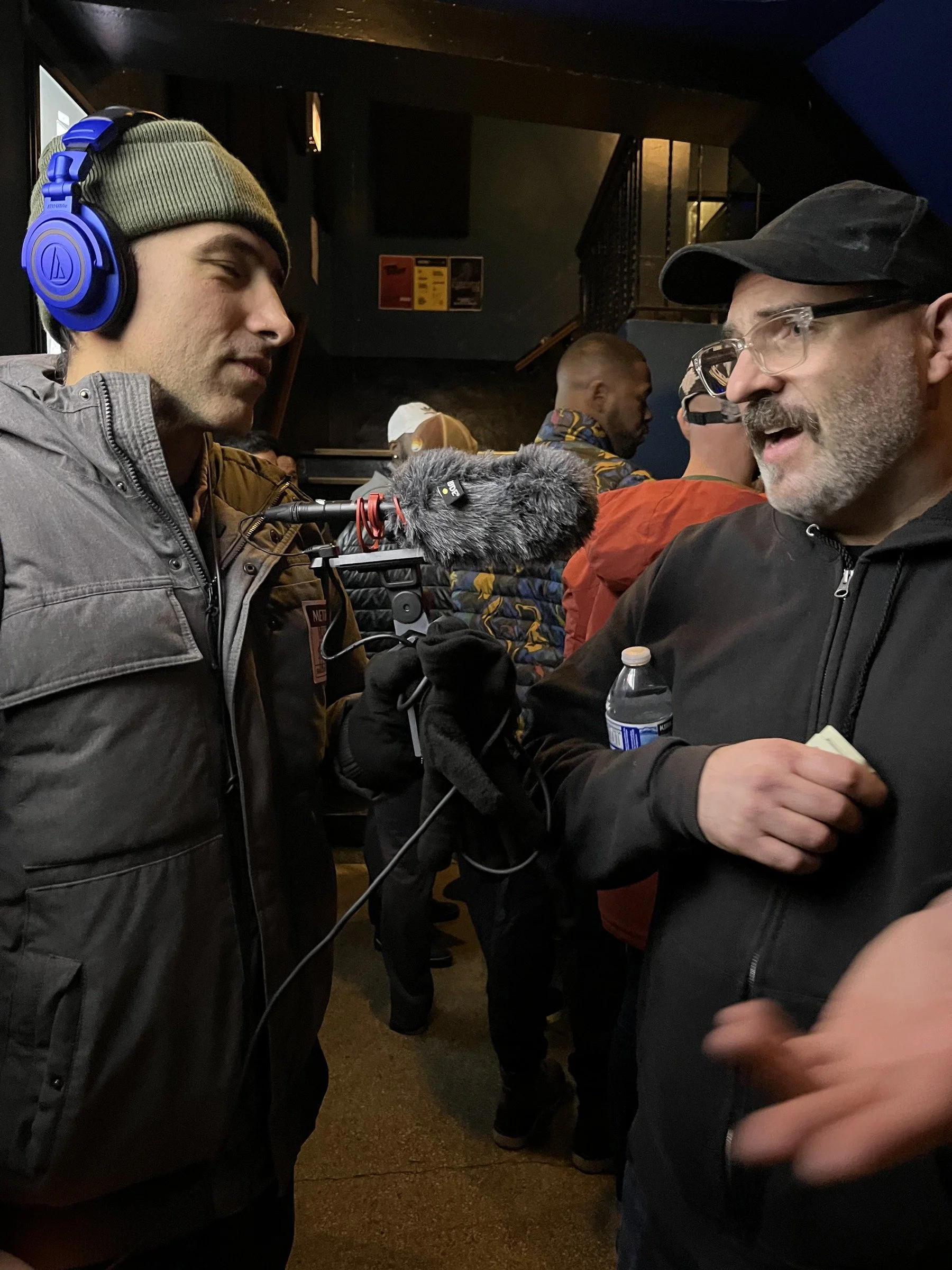 Ramtin Arablouei wearing headphones and interviewing a man with a handheld microphone.