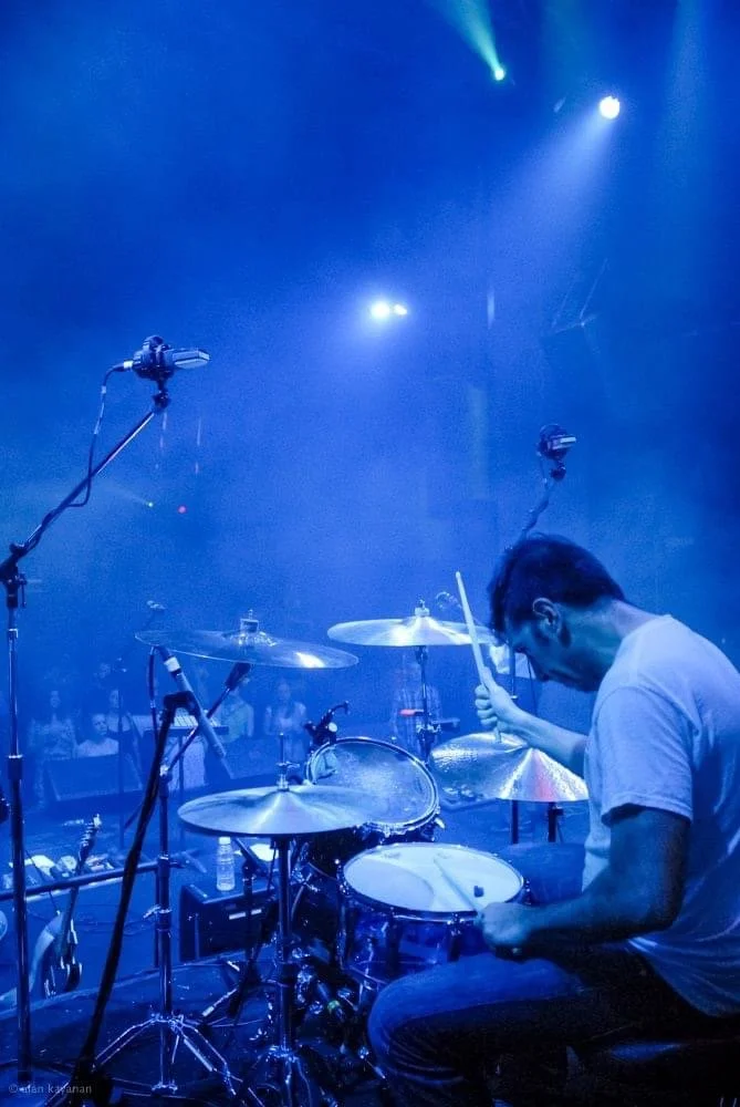 Ramtin Arablouei playing drums onstage under blue lights.