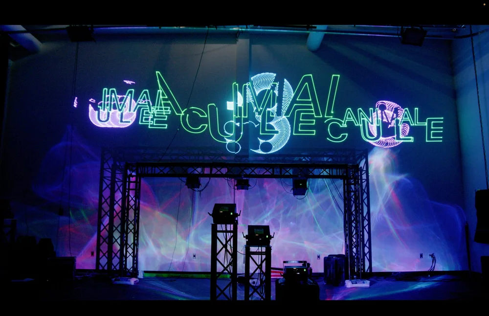 The ANIMALCULE title projected in green and violet laser light