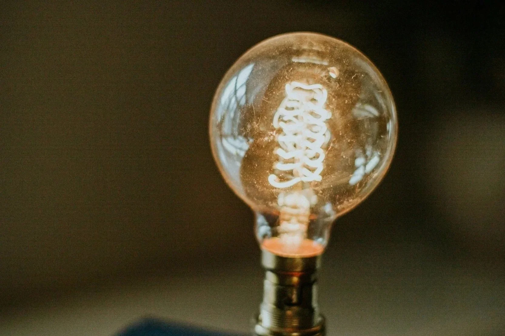 Close-up of a glowing incandescent light bulb with visible filament against a dark background.