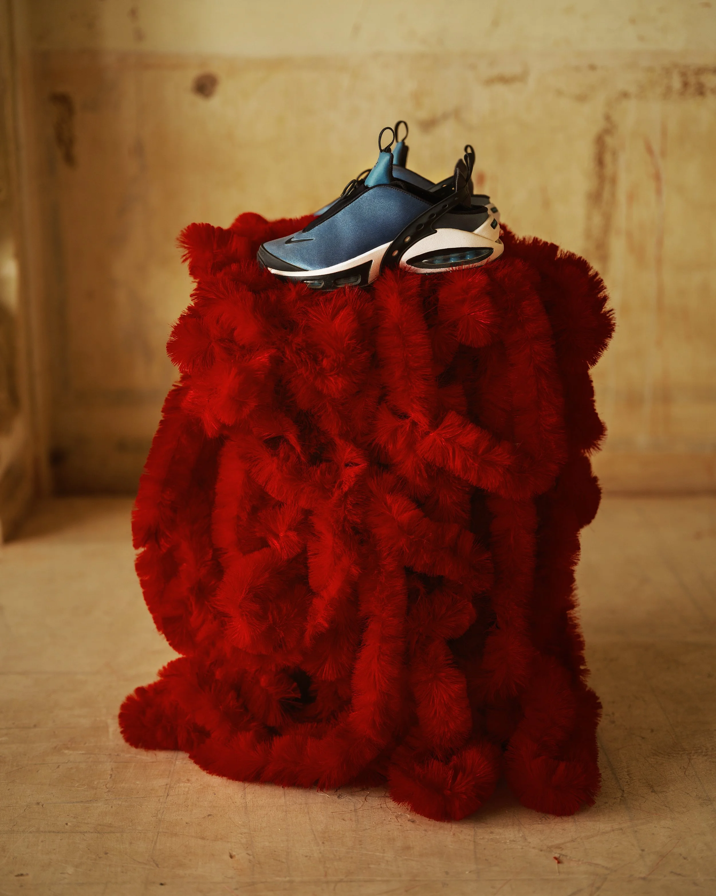 Blue and black sneaker placed on a red furry surface with a beige wall in the background.