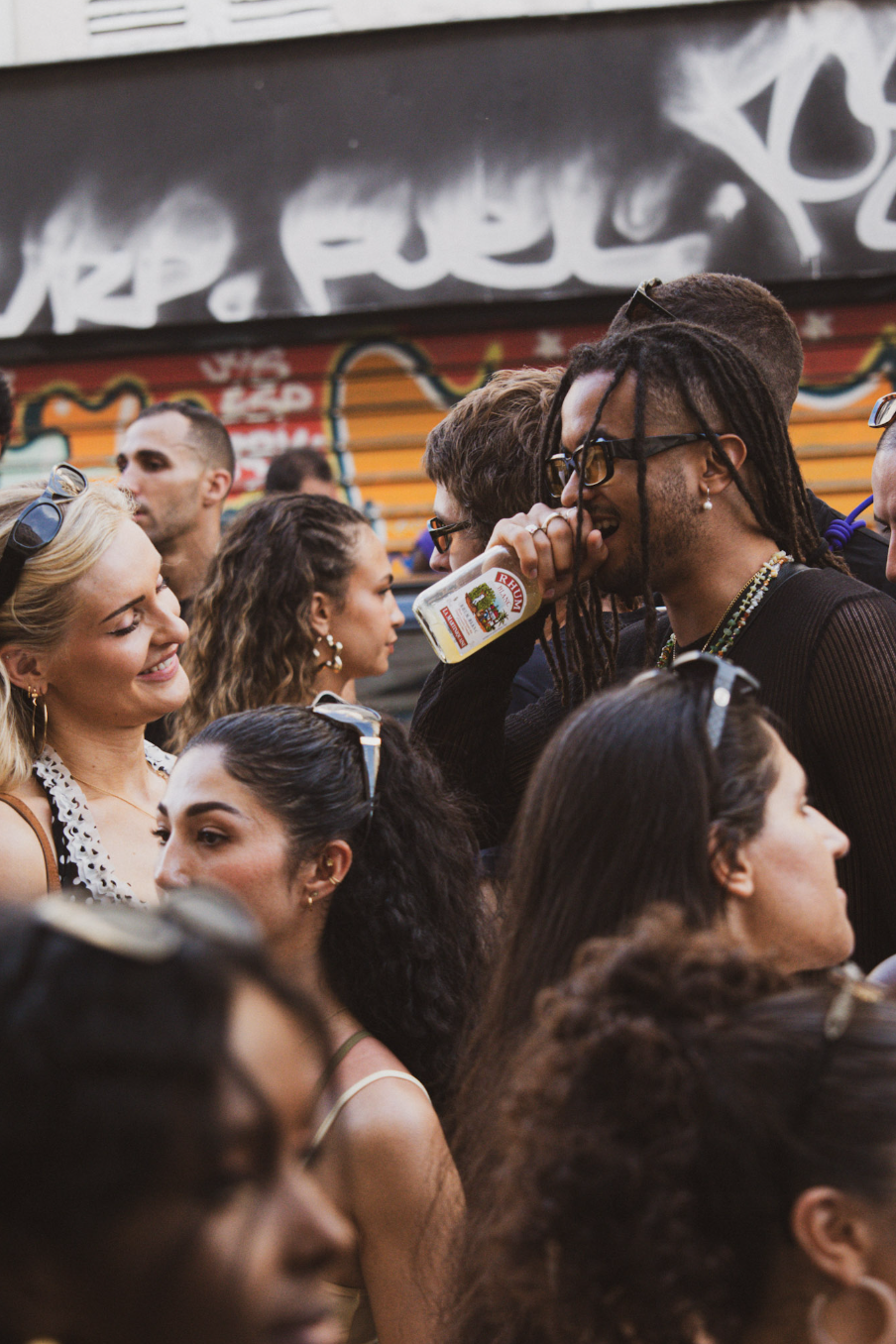 Group of diverse young adults socializing and enjoying drinks in an outdoor setting with graffiti art in the background.