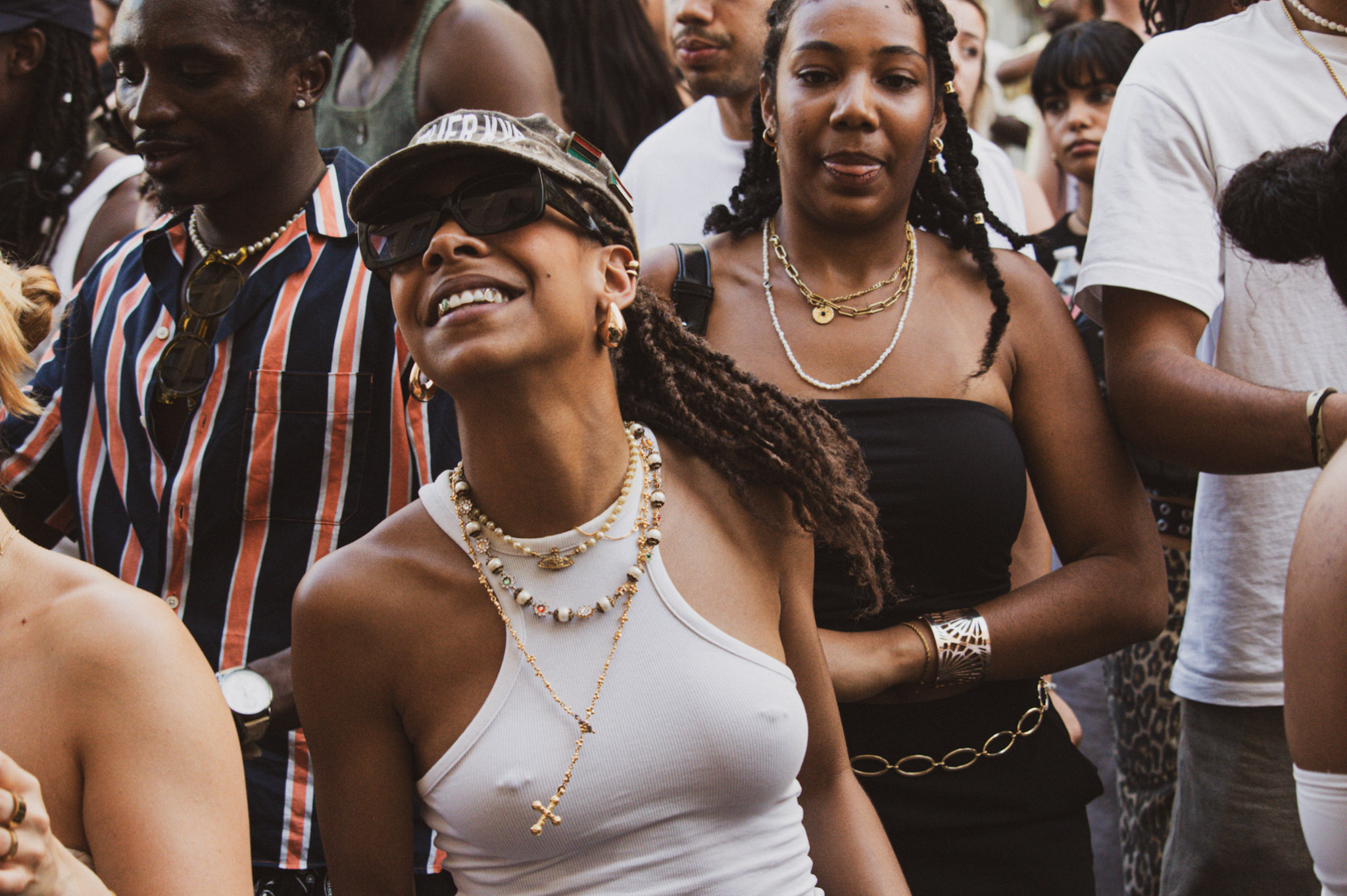 A diverse group of people at an outdoor event, with women wearing necklaces and casual clothing.