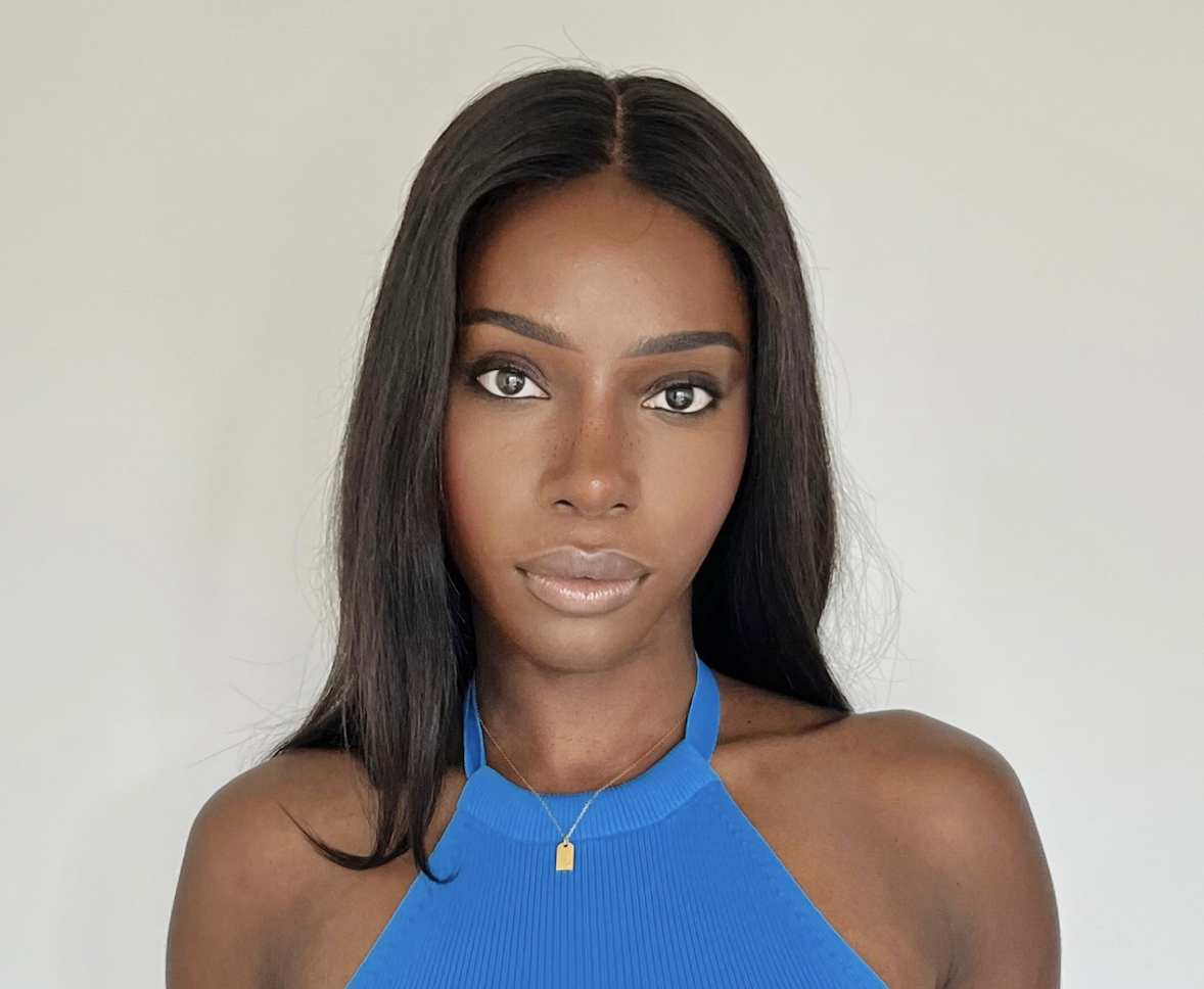 Close-up of a young woman with long black hair, wearing a blue halter top and a small gold necklace, looking directly at the camera with a neutral expression.