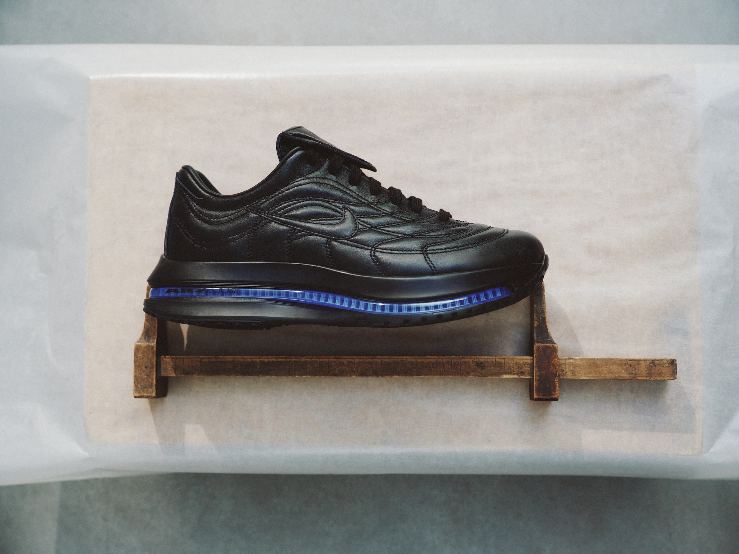A black sneaker with a blue sole displayed on a small wooden stand.