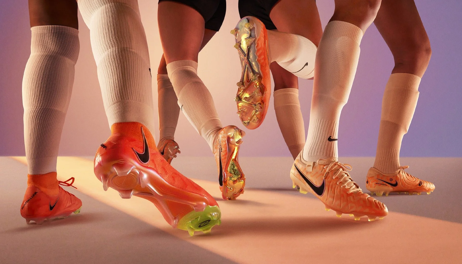 Close-up of four athletes' legs in sports attire, wearing colorful Nike soccer cleats and cream-colored socks, with a purple background.