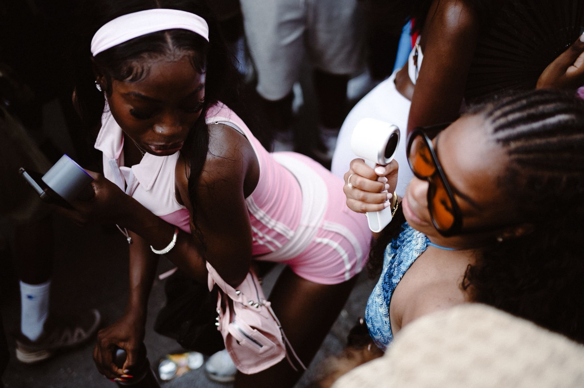 Two women are examining a handheld medical device, possibly an otoscope, while surrounded by other people in a crowded setting.