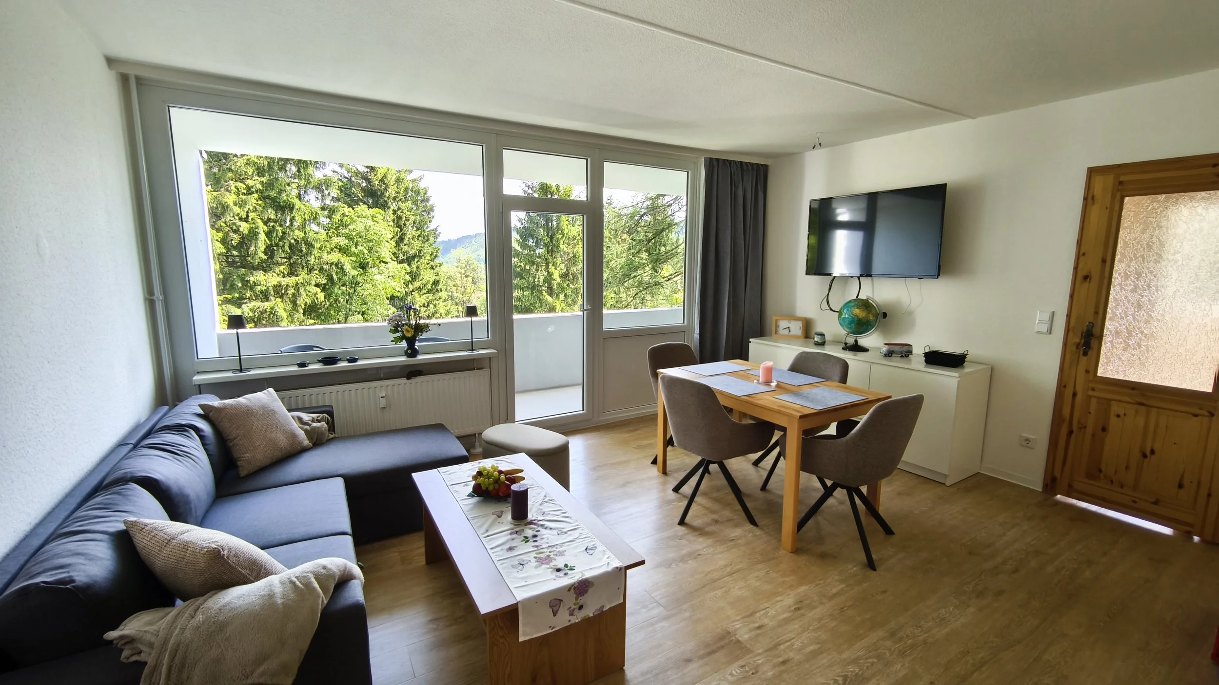Offener Wohn- und Essbereich mit Sofa, großem Fernseher und Zugang zum Balkon