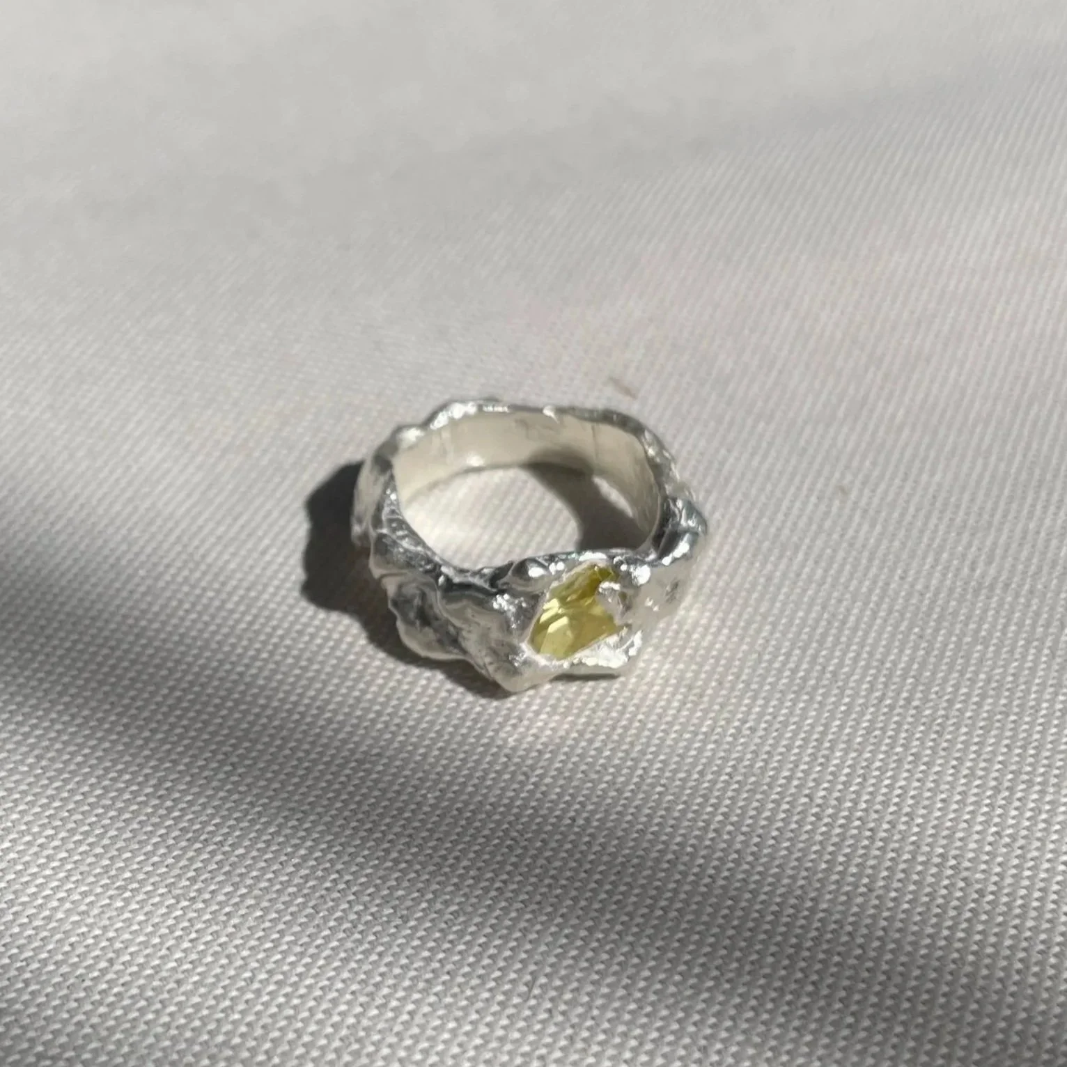 Bague en argent avec une pierre jaune en forme de cœur, posée sur un tissu blanc.