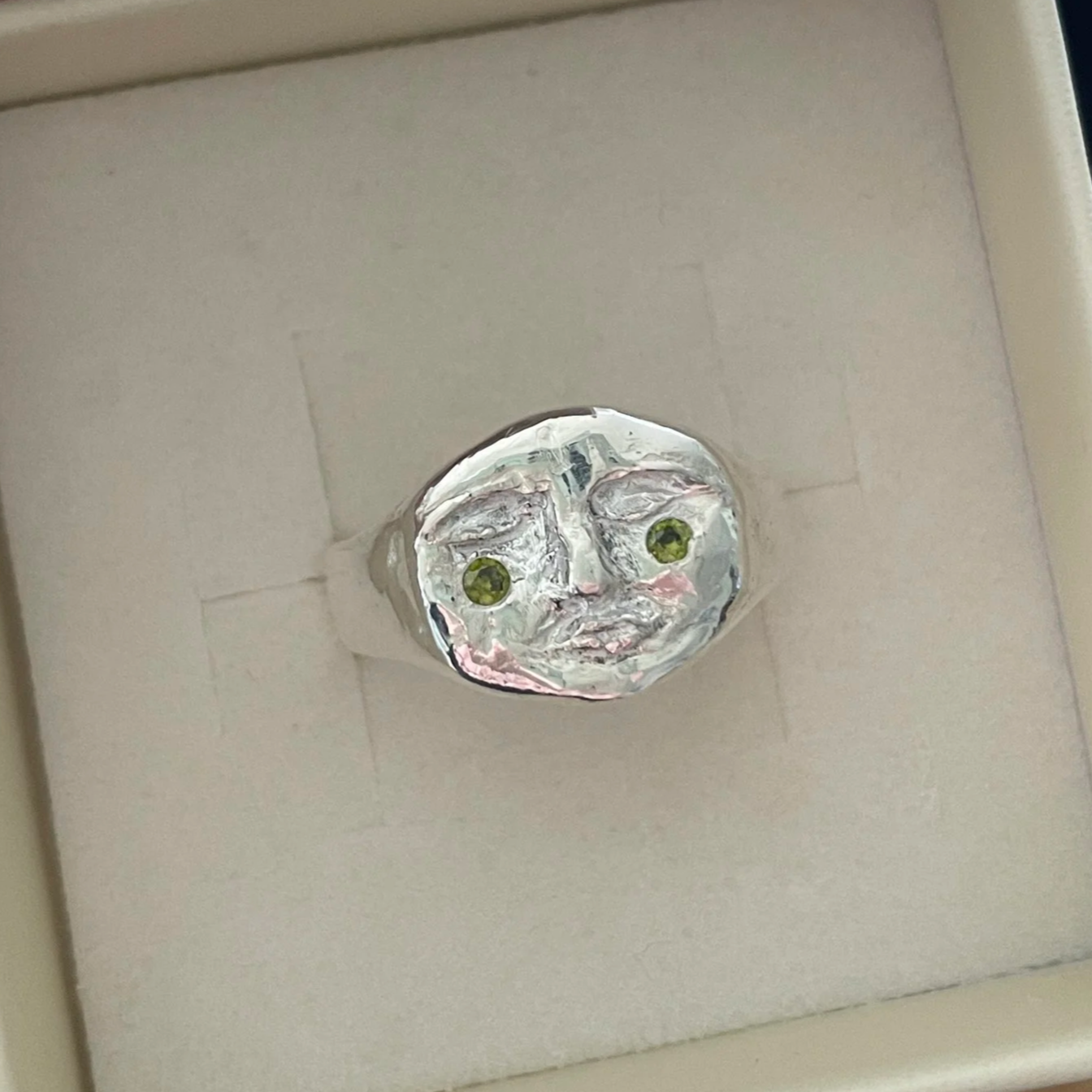Plafonnier en forme de visage humain en métal avec des yeux en pierre verte et des détails semblables à un visage.