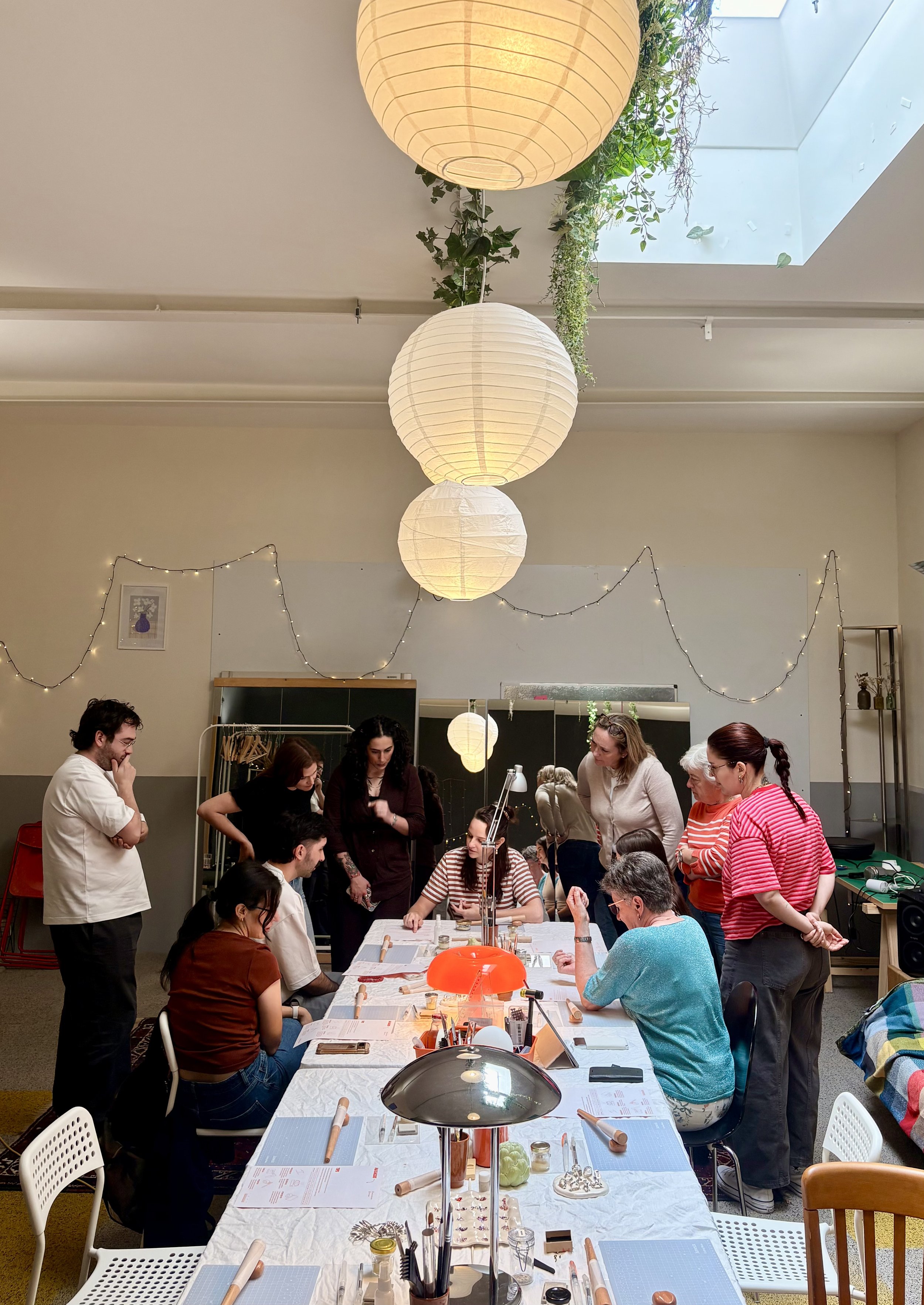 Groupe de personnes réunies autour d'une grande table en intérieur, semblant participer à un atelier ou une réunion, avec des lampes en papier suspendues au plafond et des décorations lumineuses.