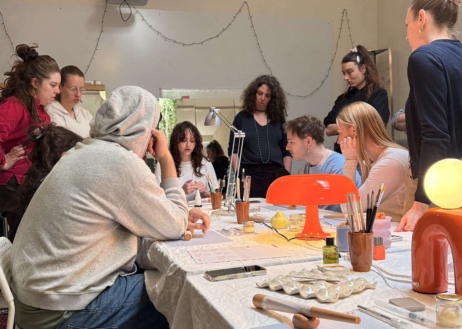 Groupe de personnes lors d'un atelier créatif, concentrées autour d'une table avec divers outils de création, accessoires et lampes, dans une ambiance chaleureuse et studieuse.