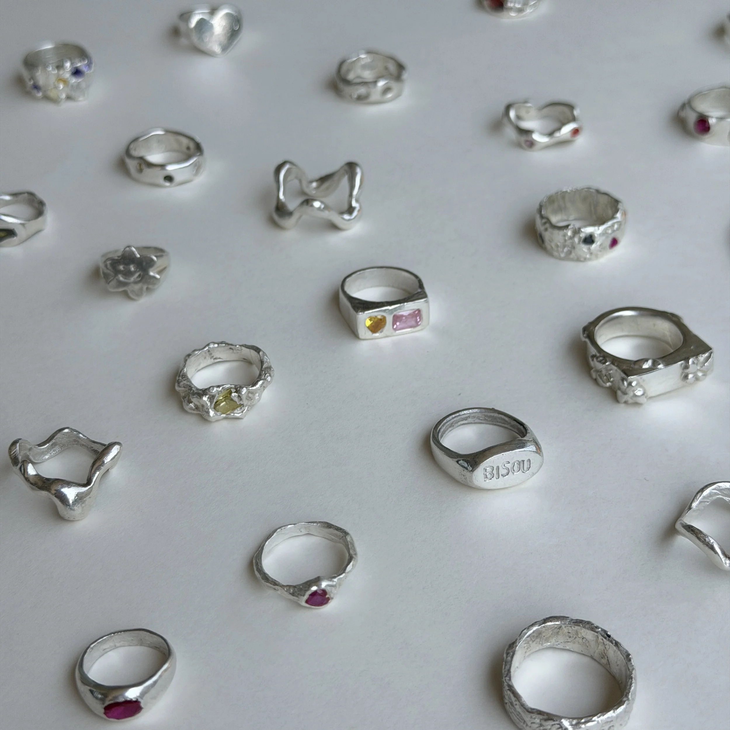 Anneaux en argent en forme de cœurs, de cercles, et avec des détails, posés sur un fond rose