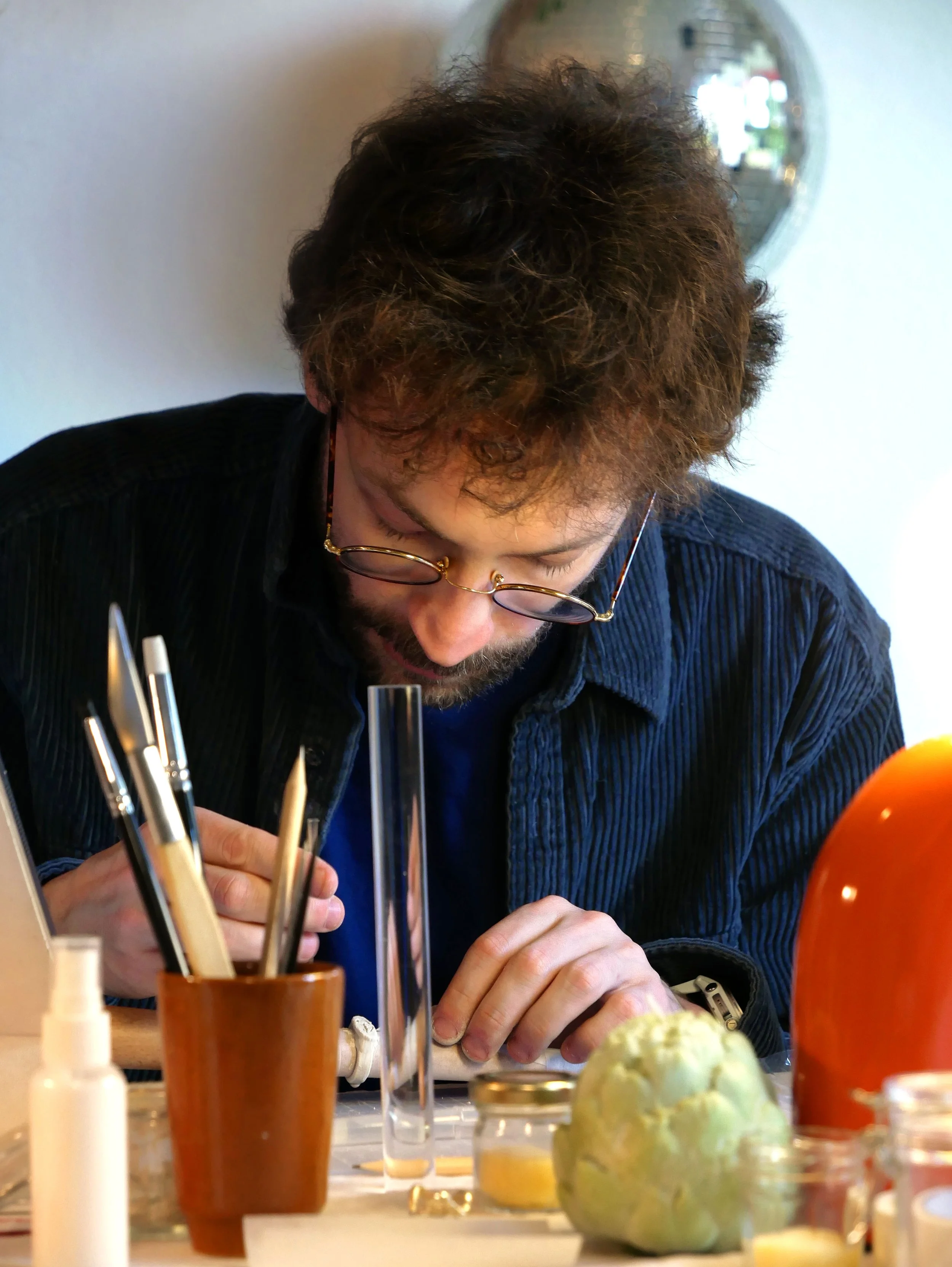 Un homme portant des lunettes regarde du matériel de laboratoire sur une table, avec des tubes à essai et des fruits exotiques visibles en premier plan.