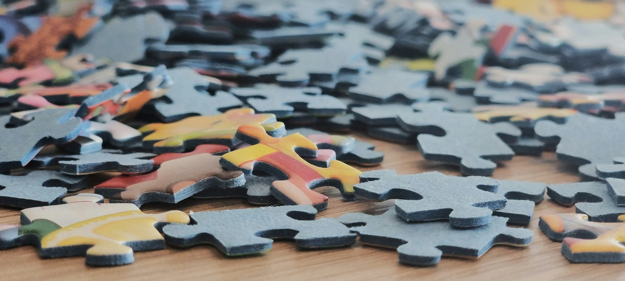 Colorful scattered puzzle pieces on a wooden surface.