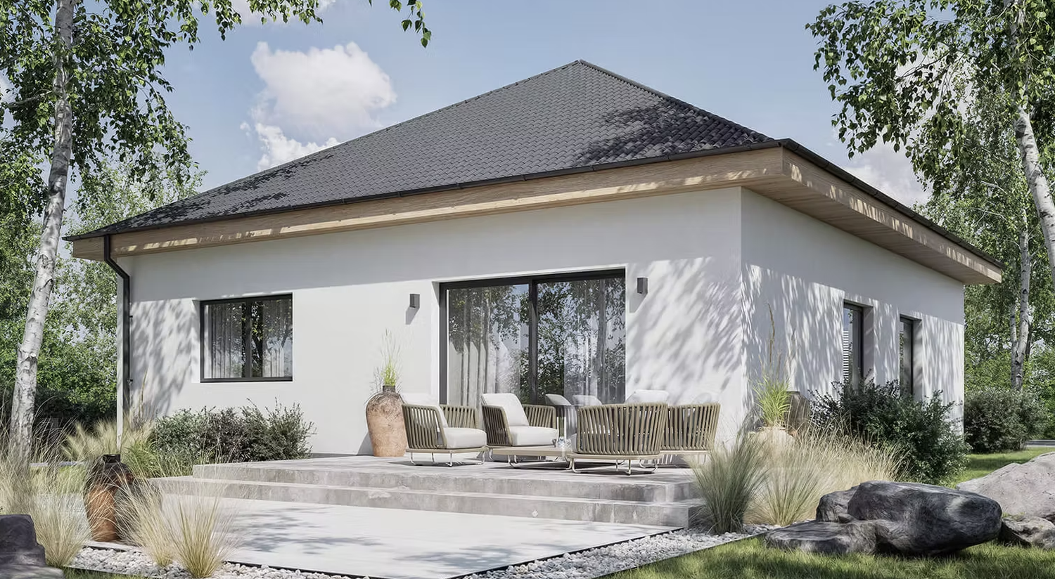 Modern white house with large sliding glass doors, a gray tiled roof, and outdoor seating on a concrete patio surrounded by rocks, grass, and trees.
