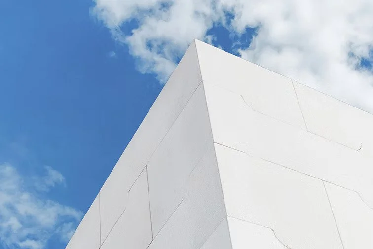 Close-up of a white modern building corner against a blue sky with clouds.