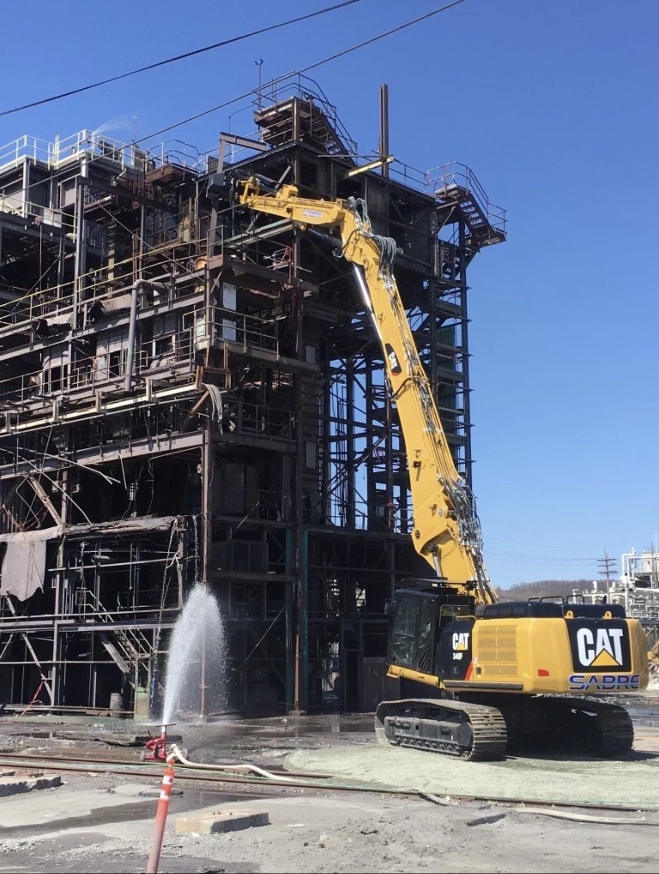 Construction site with a yellow excavator working on a multi-story building framework made of metal beams and scaffolding, with blue sky in the background.