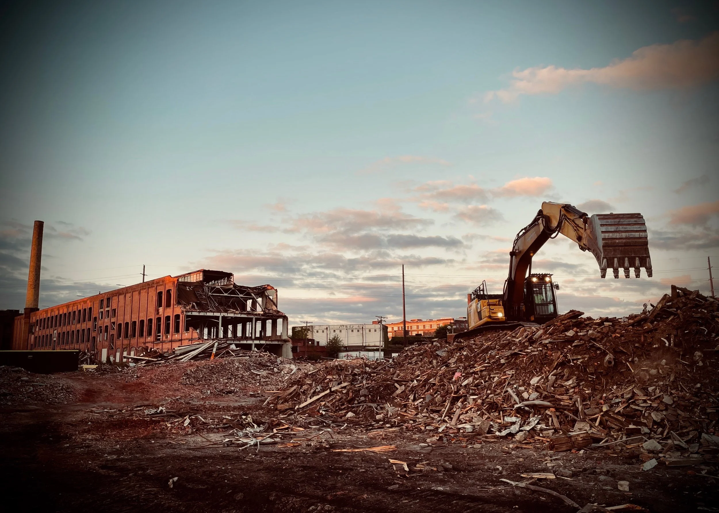 Construction site with demolished building, construction excavator, and debris during sunset.