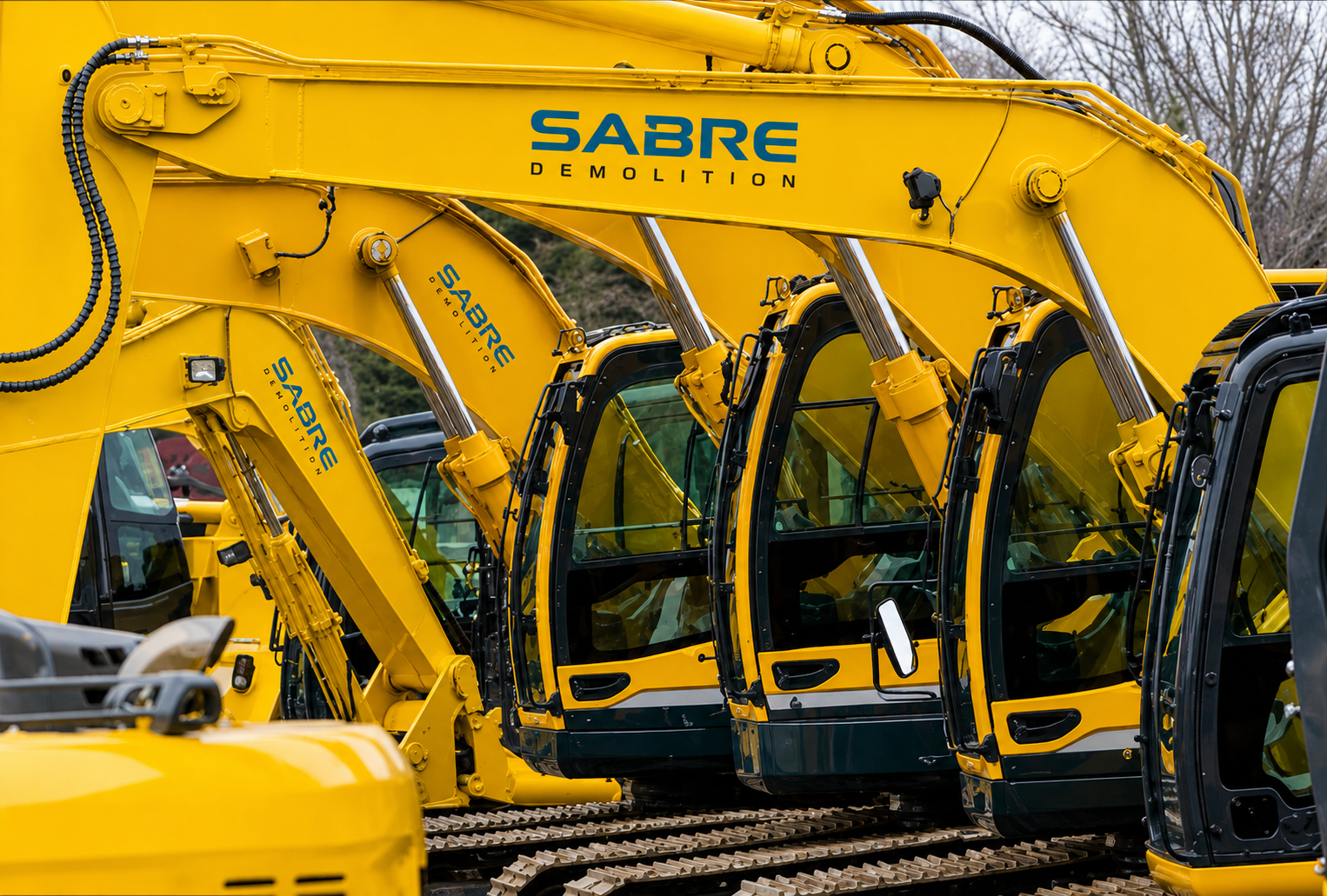 Multiple yellow excavators branded with 'SABRE DEMOLITION' are lined up outdoors, with visible hydraulic arms and glass-enclosed cabins.