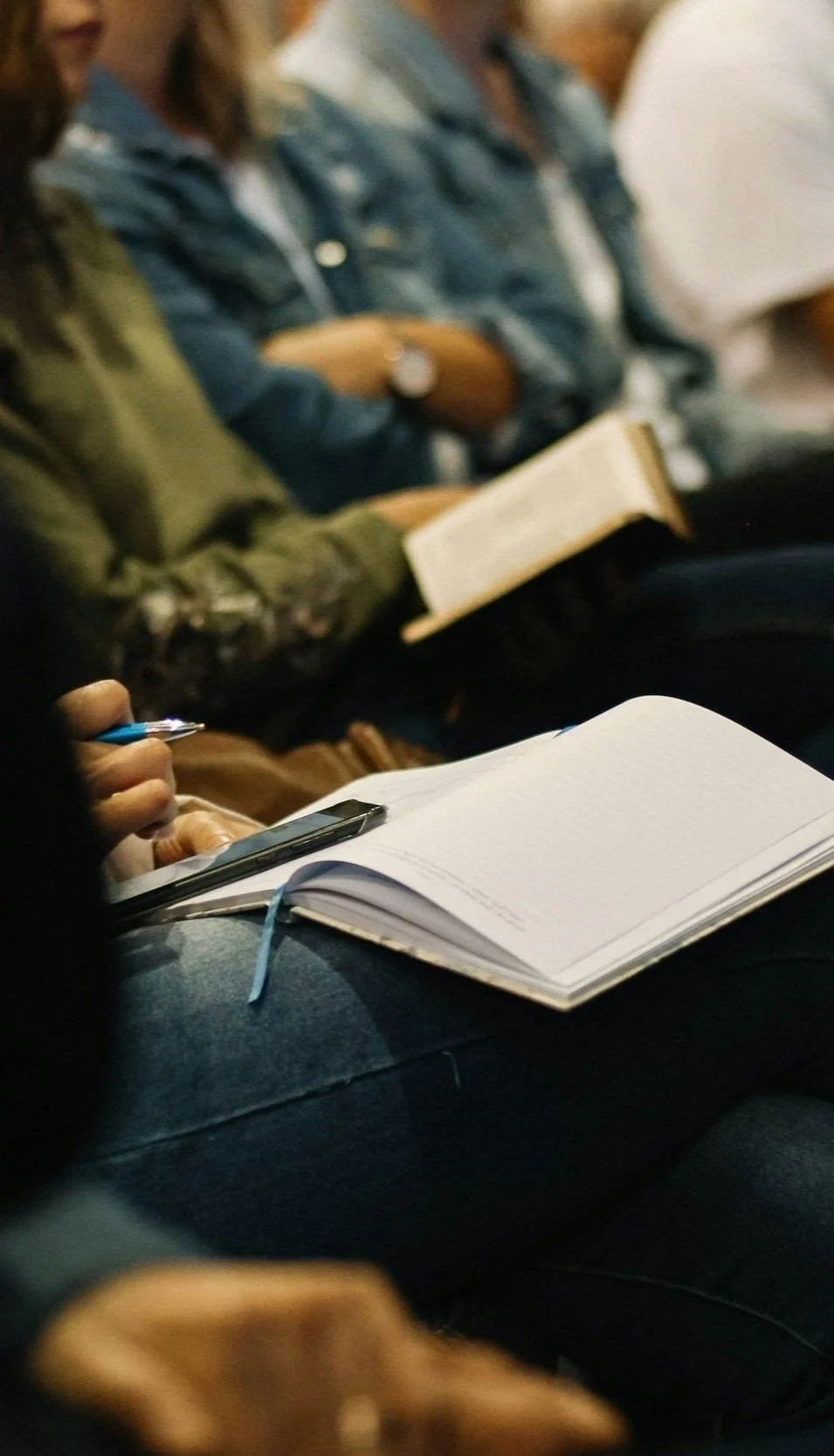 People sitting, taking notes, and reading in a classroom or lecture setting.