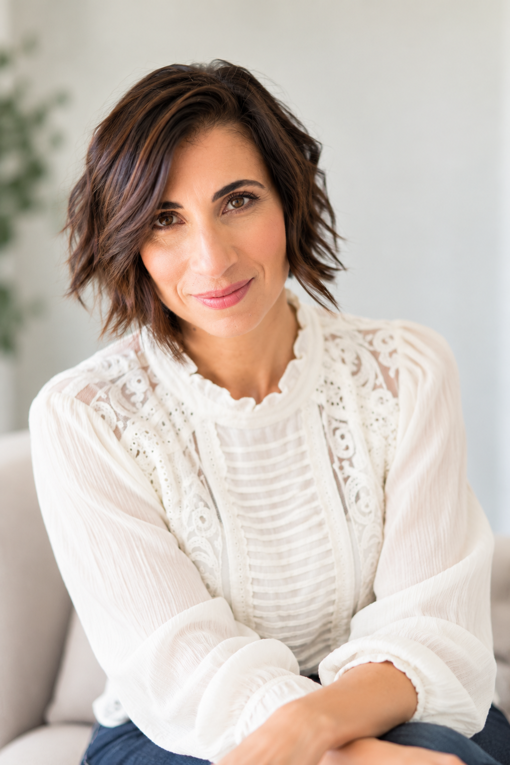 A woman with shoulder-length dark hair and a friendly smile, wearing a navy blazer over a light blouse, standing in front of a wooden wall.