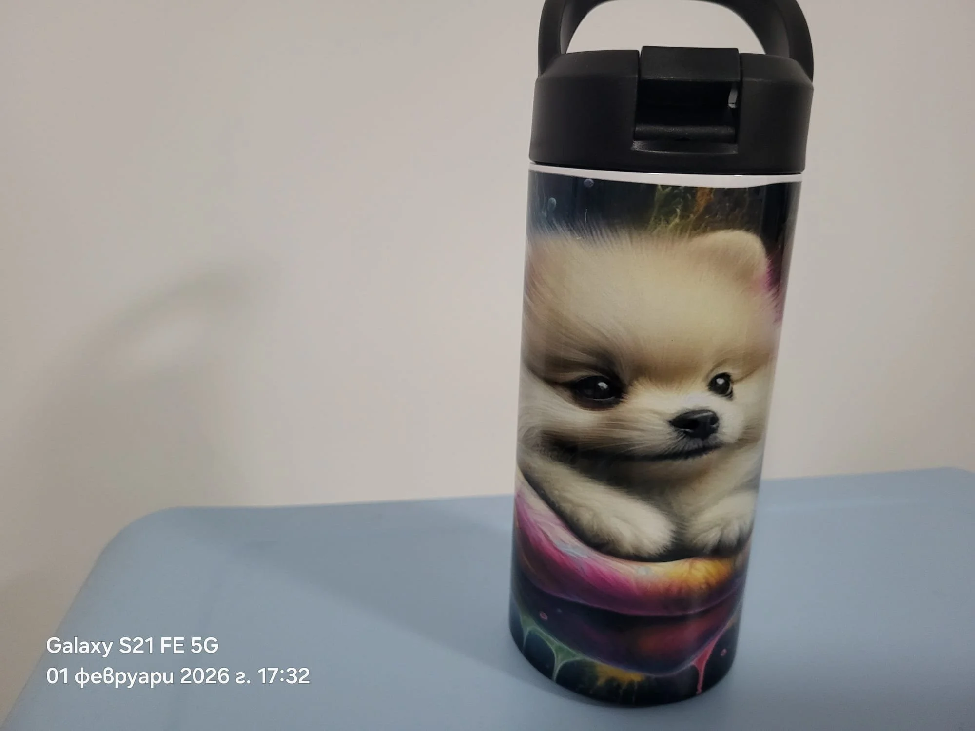 A close-up photo of a smartphone with a wallpaper featuring a cute puppy dog. The phone is placed on a white surface against a plain white background. There is a timestamp and camera information overlay on the bottom left corner.