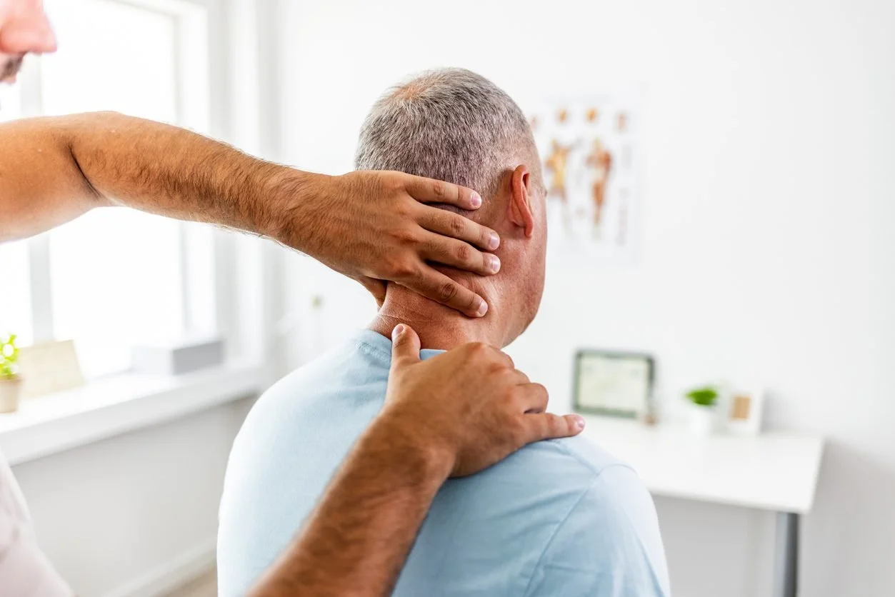 Doctor performing a neck and shoulder examination on a patient in a medical office.