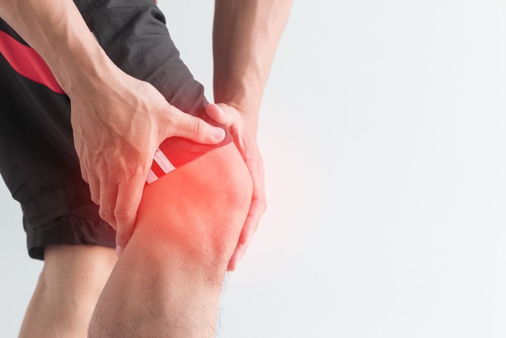 Person holding their knee with a red, irritated area indicating pain or inflammation.