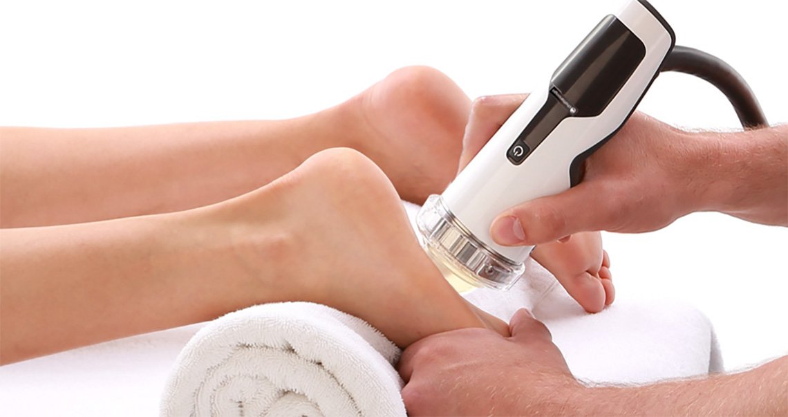 A person receiving a foot treatment with a handheld device on their foot, resting on a white towel.