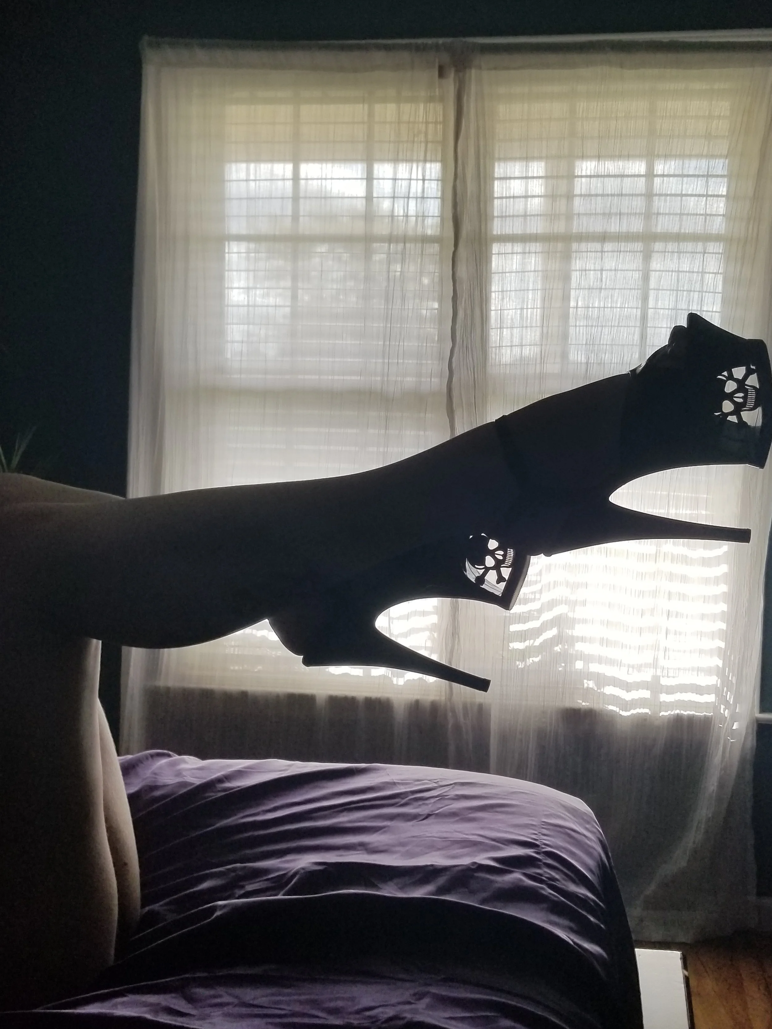 The image shows a person lying on a bed with a black metal headboard, in a room with large windows covered by sheer curtains, allowing light to come through.