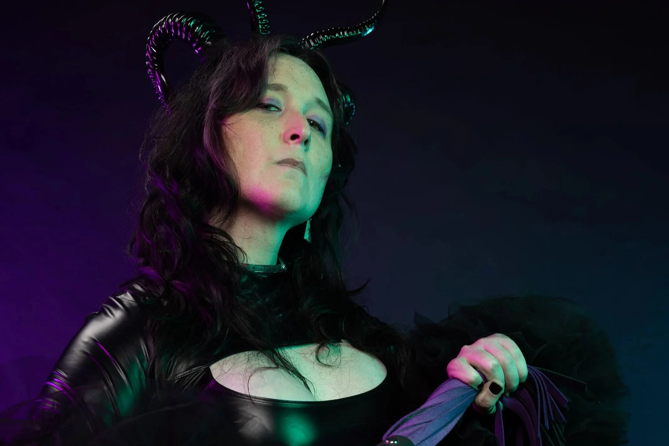 A woman wearing black leather clothing and black gloves, holding a sword, with a dark outdoor background at night.