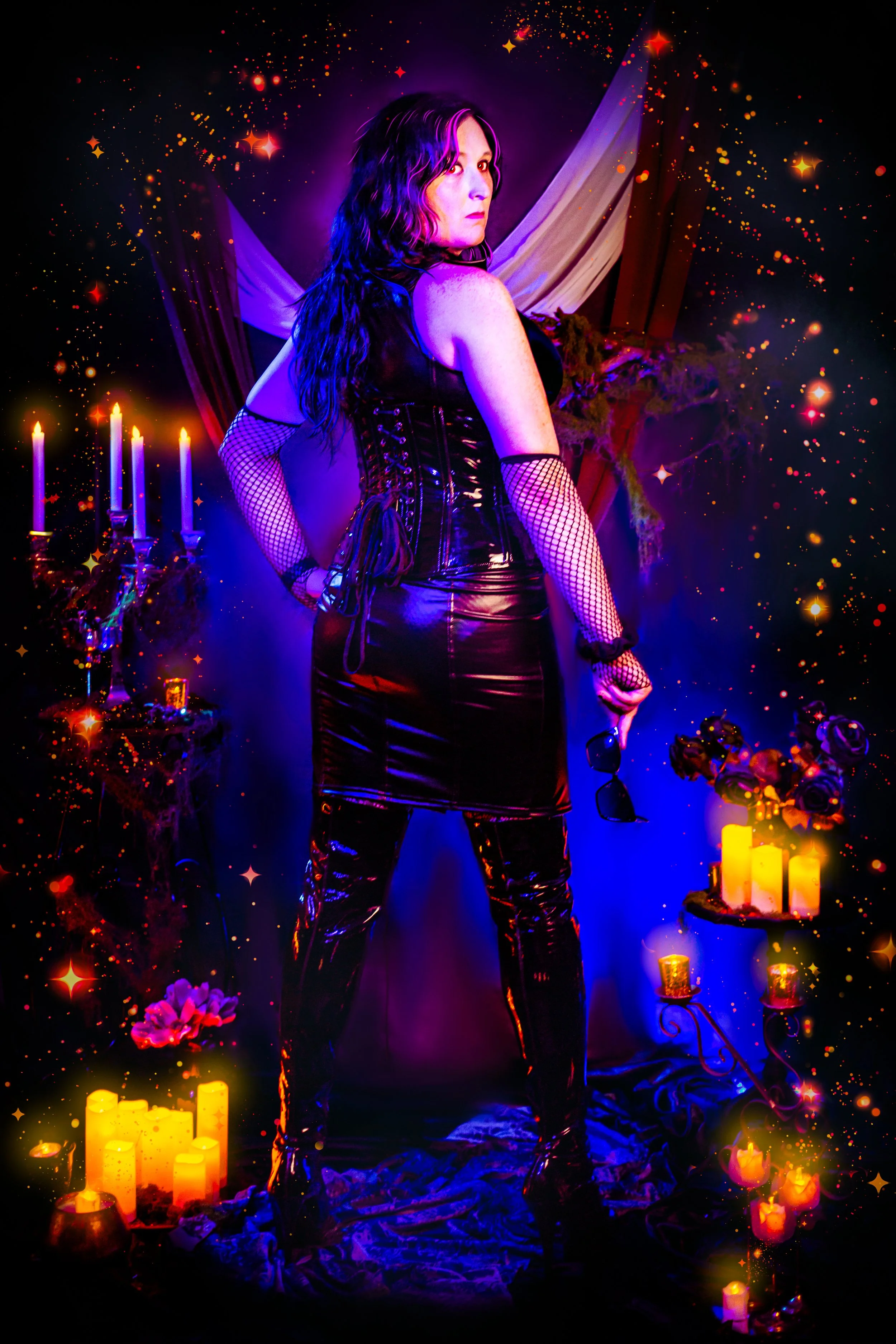 A person with long dark hair wearing a black leather outfit and fishnet gloves stands in a room decorated with candles, flowers, and draped fabrics, illuminated by purple and warm candlelight, with sparkles and stars overlaying the scene.